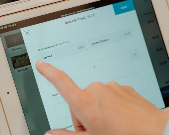 Close-up of a person's finger interacting with a point of sale tablet screen.