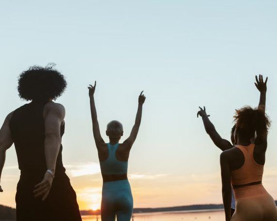Group of diverse individuals exercising at sunset by a lake, embracing fitness and nature.